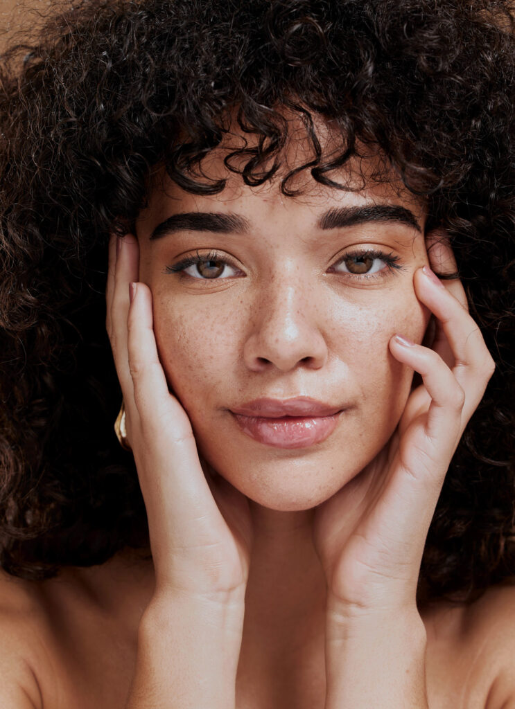 Woman smiles directly into camera and holds her face.