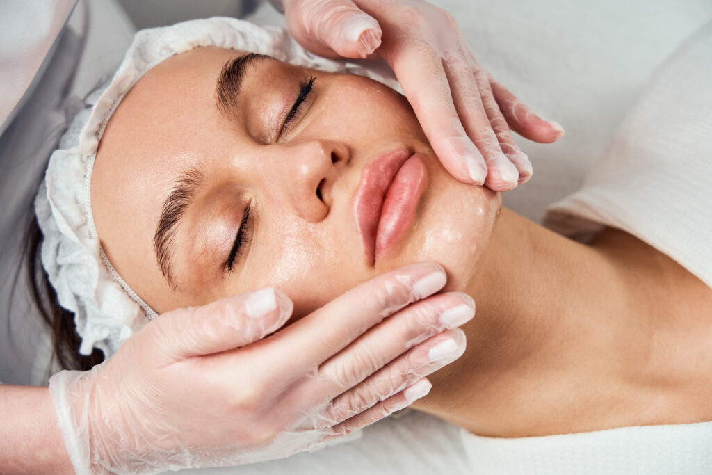 Patient lying down with eyes closed as professional wearing gloves gives her a facial.