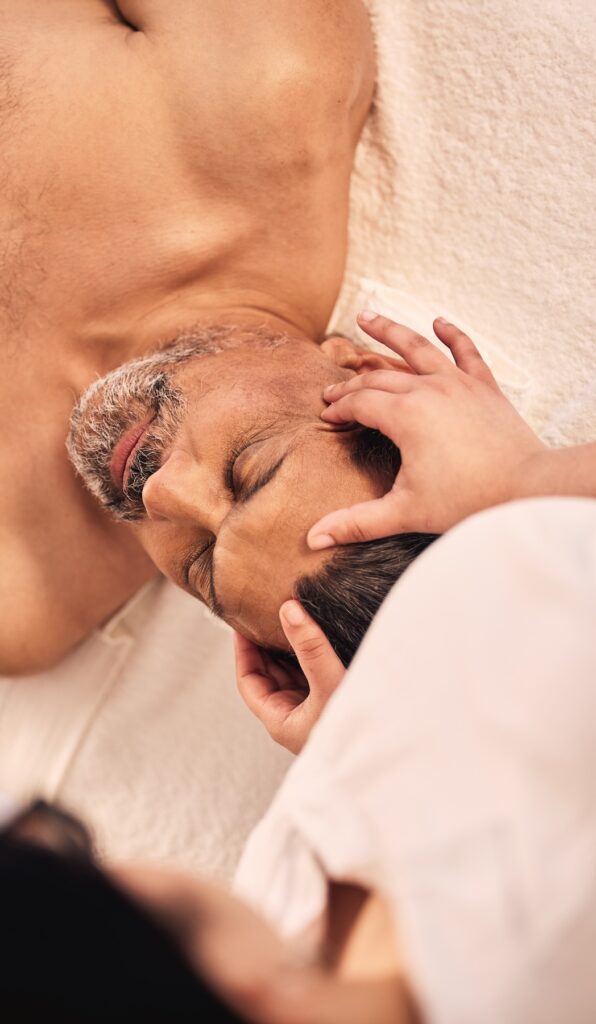 Young professional massages man's forehead as he reclines.