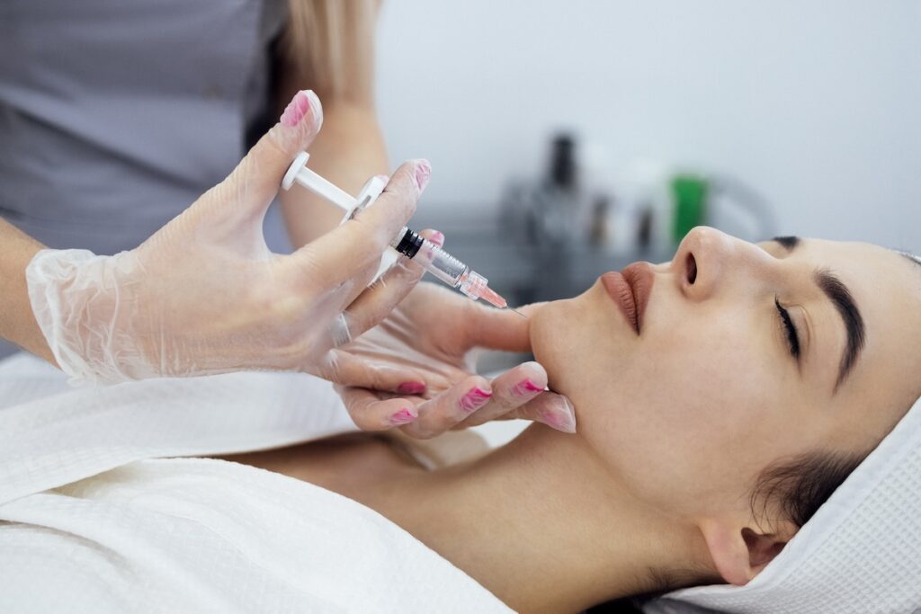 Woman lying down as nurse injects her chin with filler.