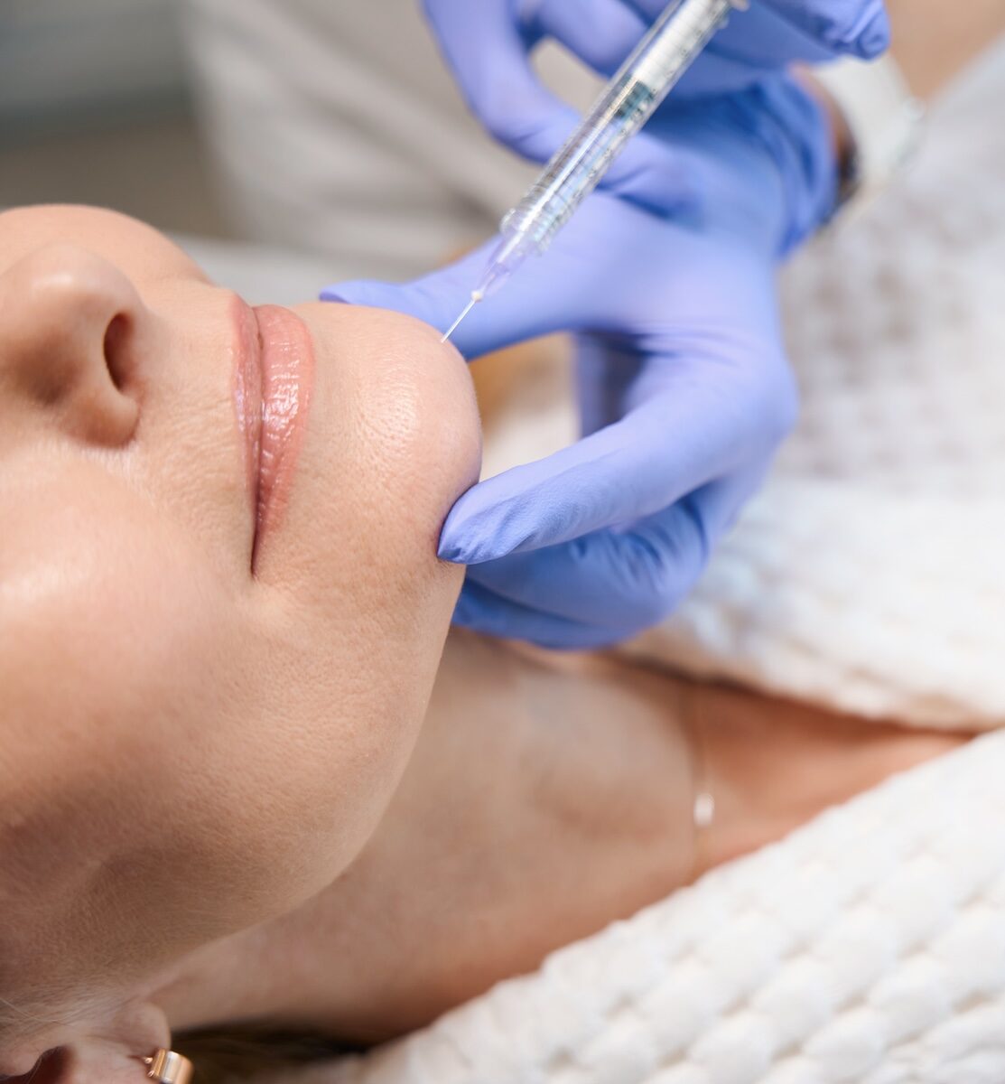 Close up of woman's chin with a needle in it for filler or Botox.