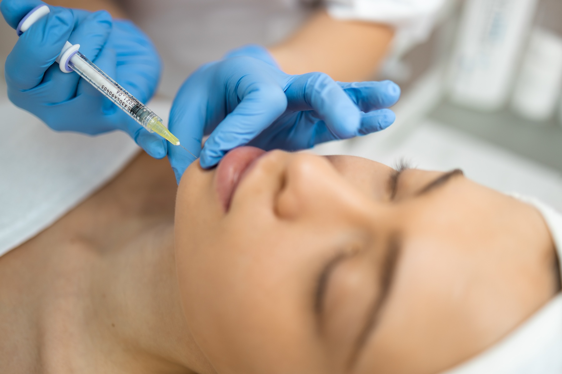 Woman lying down as professional wearing gloves injects needle into her chin.