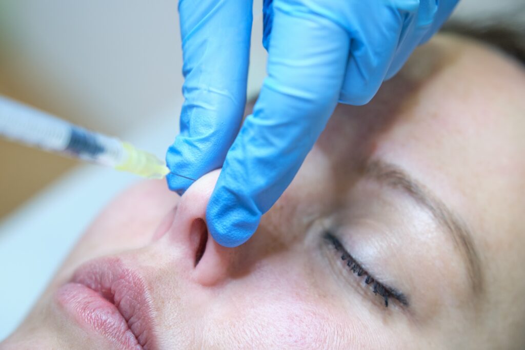 Professional holding patient's nose tip to inject nose filler.