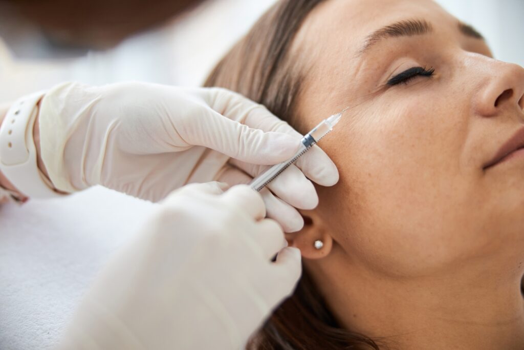 Side angle of woman with eyes closed as nurse holds needle next to her eye
