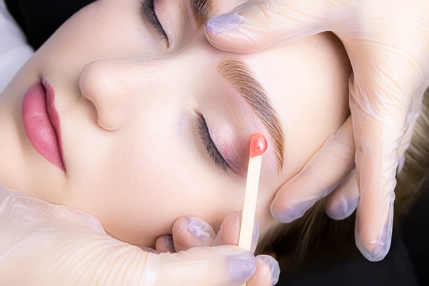 Wax on wooden spoon applied to woman's eyebrow