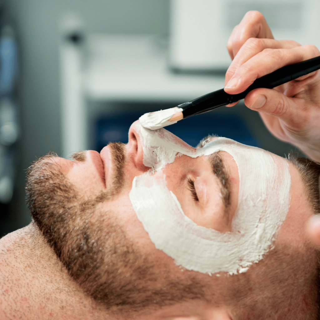 Close up of a facial mask is being applied to a man with a brush while his eyes are closed