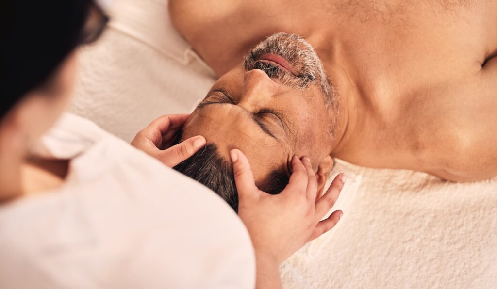 A female provider at Exhibit Medical Aesthetics massaging the forehead of a male patient as a part of their treatments for men's skincare in Denville.