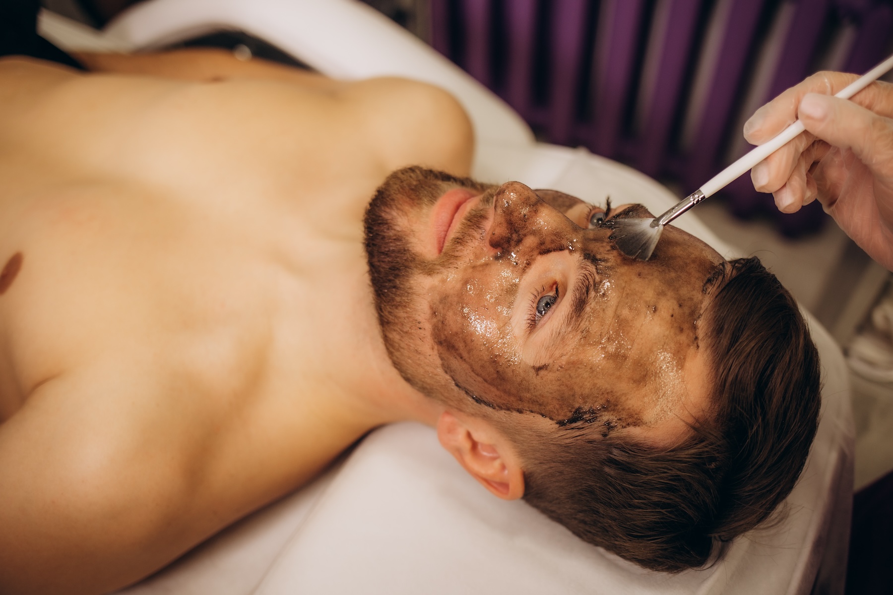 men's cosmetology. the doctor is a cosmetologist in a white robe, wearing gloves, puts a mask on the man's face. High quality photo