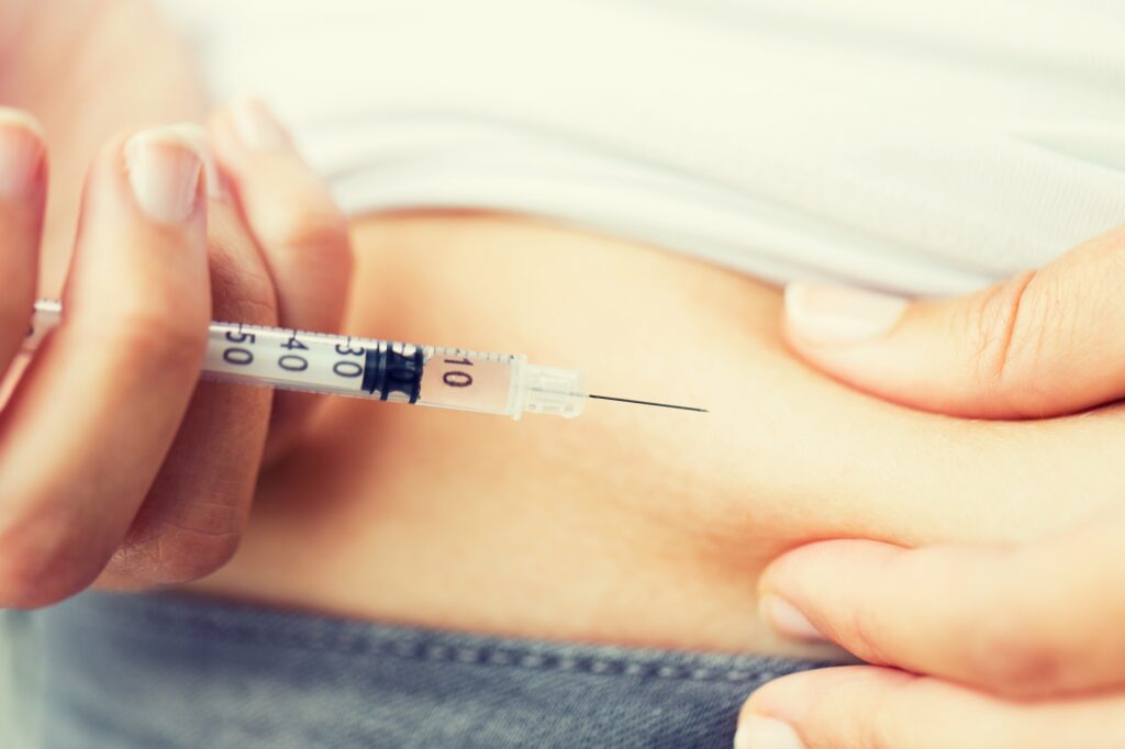 medicine, diabetes, glycemia, health care and people concept - close up of woman with syringe making insulin injection to himself at home