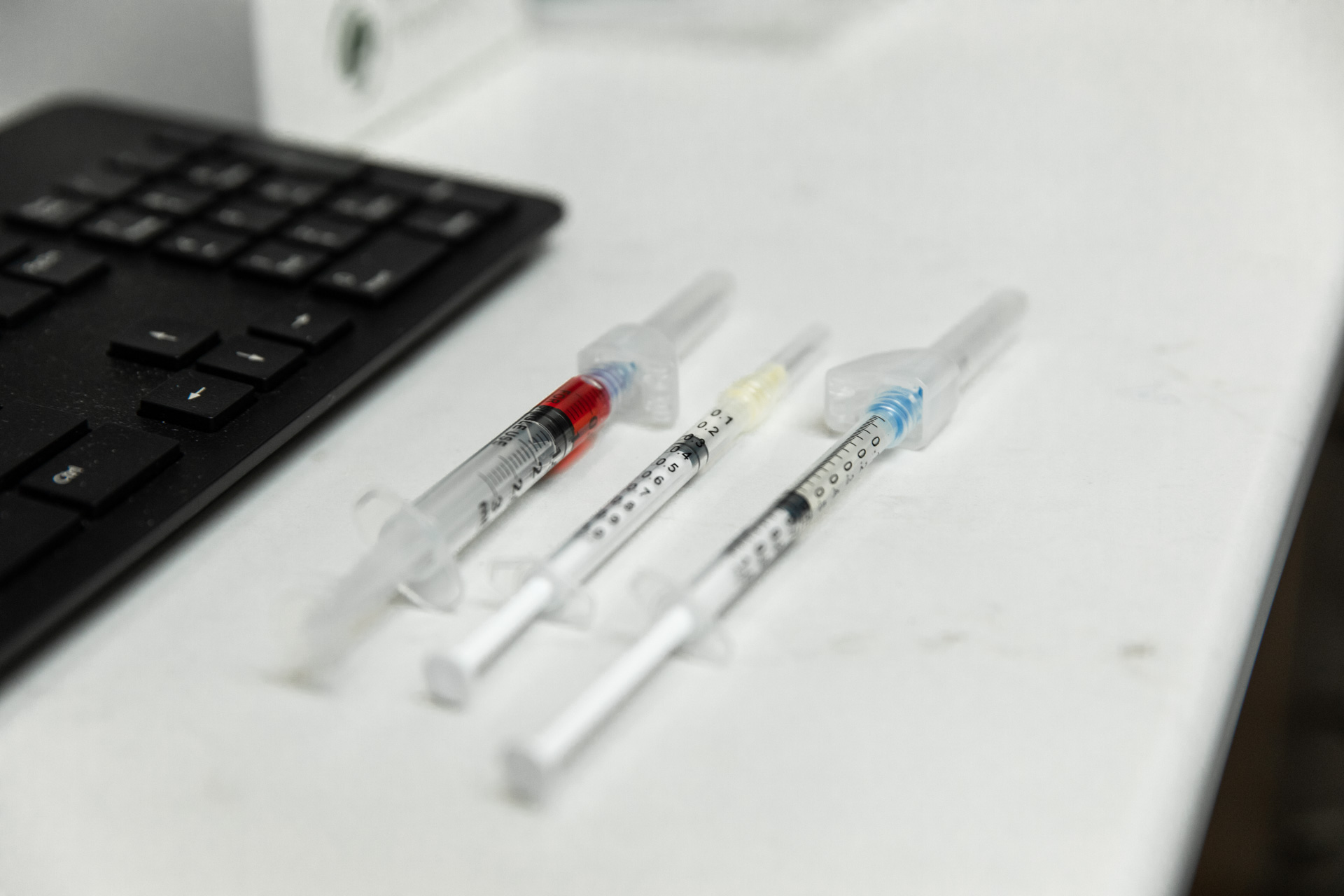 Three different types of vitamin injections laid out on desk next to keyboard.