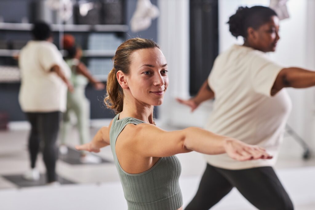 Young woman in sportswear working out in health club with other women in background