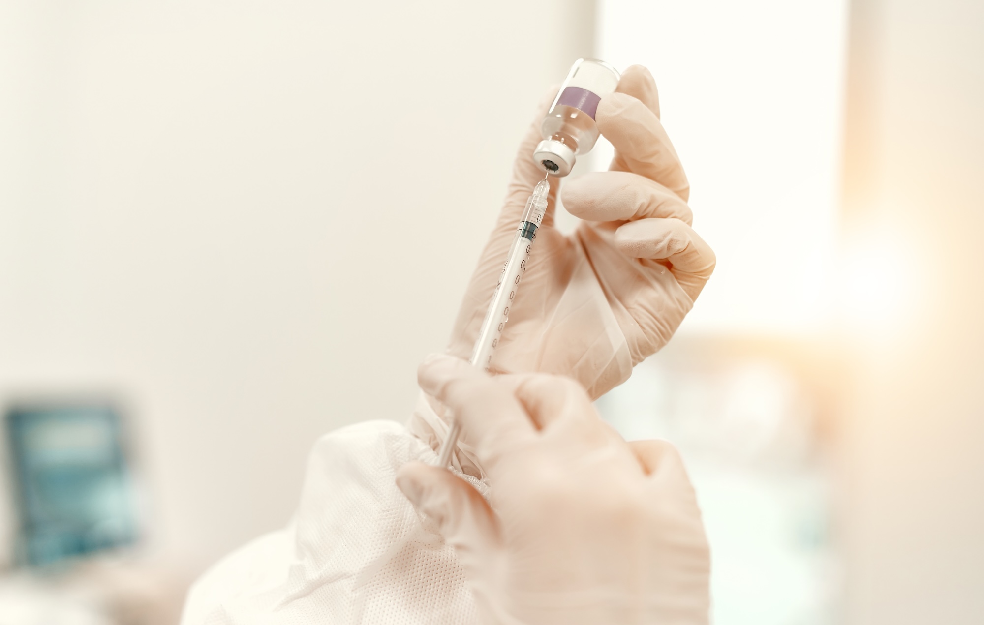 A doctor in a protective suit holds a syringe and an ampoule with the covid-19 coronavirus vaccine while standing in an intensive care unit in a modern hospital.