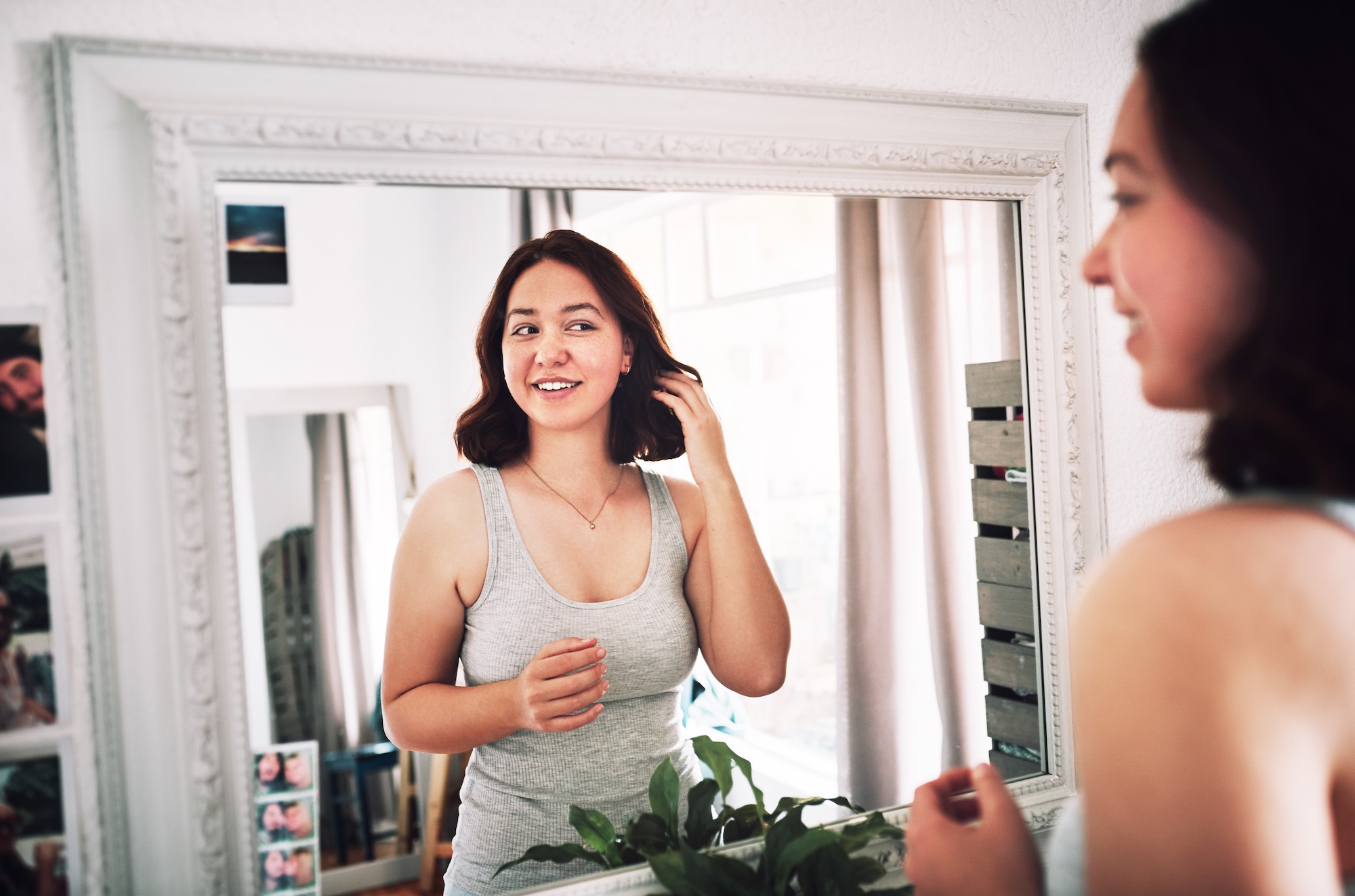 A young woman looking into the mirror at home, happy with the results she was able to achieve after visiting the team at Exhibit Medical Aesthetics for Sculptra in Morris County.
